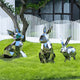 Three Coco II Rabbit Steel Outdoor Sculptures from Giant Sculptures, each featuring a minimalist rabbit design, enhance the vibrant green grass. They stand proudly against a white picket fence and a modern building with large windows, as trees with lush foliage sway nearby.