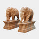 Two Elephant Yellow Marble Outdoor Sculptures by Giant Sculptures are depicted, each on a rectangular pedestal. These 180cm outdoor sculptures feature intricately carved elephants adorned with decorative back patterns, showcasing detailed craftsmanship.