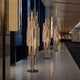 A modern hallway features polished floors and tall sculptural lamps with vertical metallic rods providing warm light. Recessed ceiling lights add to the ambiance, while large windows enhance the spaces aesthetic, akin to Giant Sculptures Strata Copper Abstract Steel Sculpture (165/220cm).