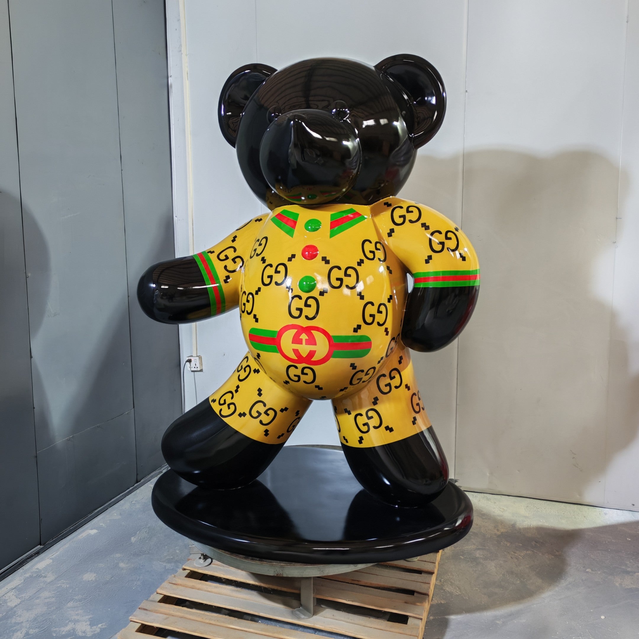 The Gacko Gucci Bear Sculpture - 165cm by Giant Sculptures features a black head, arms, and legs with a yellow GG-logoed outfit and red-green stripes—a glossy pop art piece perfect for indoor display.