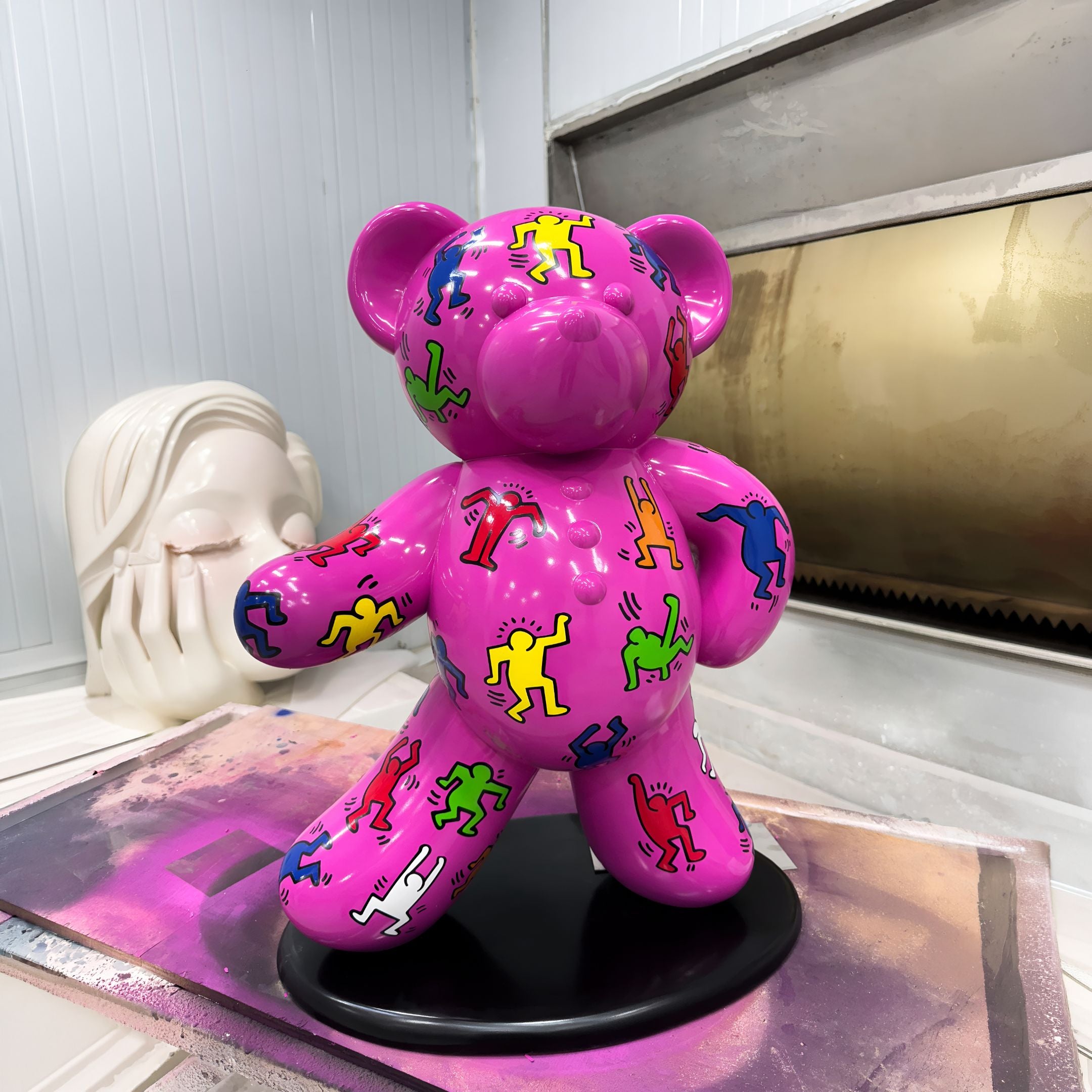 Gacko Keith Haring Pink Bear Sculpture, 70cm glossy fibreglass bear with colourful dancing figures on a black base, in a workshop setting.