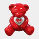 The Gacko Love Bear Sculpture - 160cm by Giant Sculptures is a shiny red teddy bear inspired by André Gacko’s pop art, sitting with legs spread, holding a white heart outlined in red with "Love" in black cursive.
