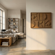 Formate Golden Bronze Geometric Wood Painted 3D Wall Art by Giant Sculptures mounted on a cream wall in a Nordic living room with a linen sofa and bookshelf.