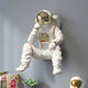 The White Astronaut Thinker 3D Wall Art by Giant Sculptures, a sleek figure in a spacesuit and helmet, sits on a shelf beside books, an astronaut helmet model, and a succulent plant, capturing space exploration with whimsical flair.