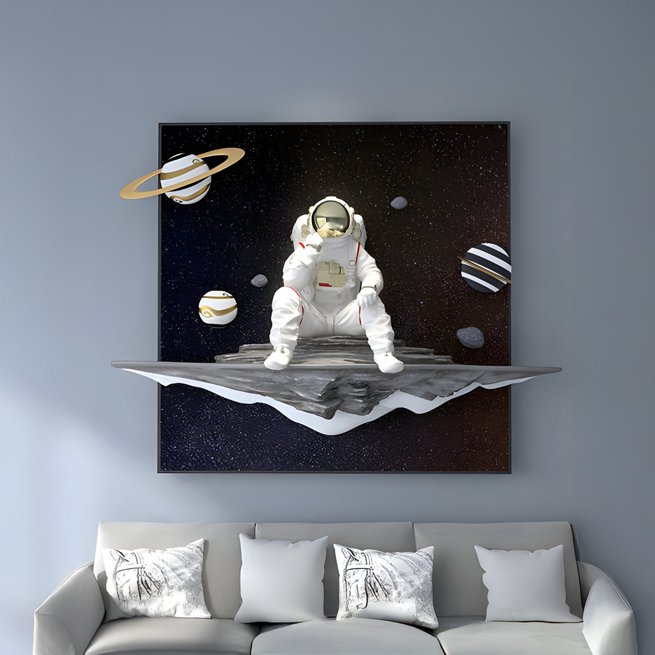 The White 3D Galaxy Astronaut Thinker Starry Wall Art by Giant Sculptures features an astronaut on a floating platform with planets and stars, elegantly displayed above a light gray couch with patterned pillows against a gray wall.