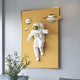 Giant Sculptures White 3D Solar Astronaut Golden Portal Wall Art showcases an astronaut floating in space amid a golden backdrop, planets, including a ringed one, and a small foreground plant, creating the perfect space décor.