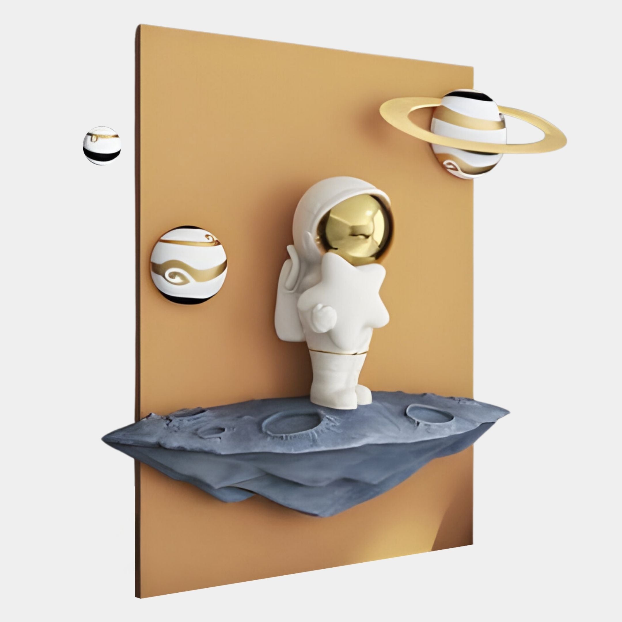 The Giant Sculptures White 3D Stardust Astronaut Wall Art features a resin astronaut holding a star on a rocky base, with two gold-ringed planets and a brown rectangular backdrop for a cosmic décor touch.