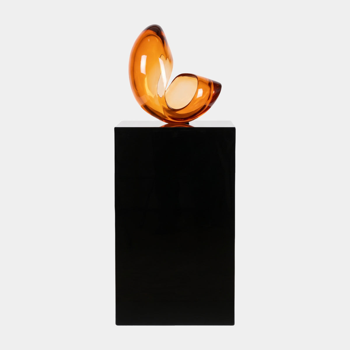 Amber Unequal Twin-Lobe Resin Sculpture, glossy orange twin-lobe form on a tall black marble plinth, set against a plain white background.