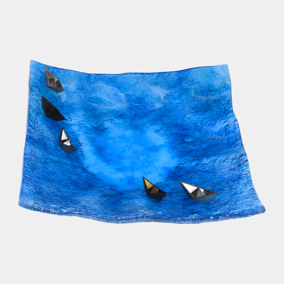 Blue Folded Boat Basin Panel Resin Sculpture, 44cm, a wavy-edged dished panel in deep blue with five black and gunmetal folded boats, one gold-toned, on a plain background.