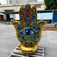 Giant Sculptures' 150cm Golden Hamsa Hand Protection Sculpture in cobalt blue and gold fibreglass with central eye motif, displayed on a pallet in an outdoor workshop yard.