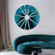 A modern living room highlights a teal semi-circular couch, a geometric radial-segmented mirror in aqua, and Giant Sculptures Halo Aqua Segment Circle 3D Metal Wall Art. A slender floor lamp complements taupe curtains, while a black side table adds a contemporary touch.