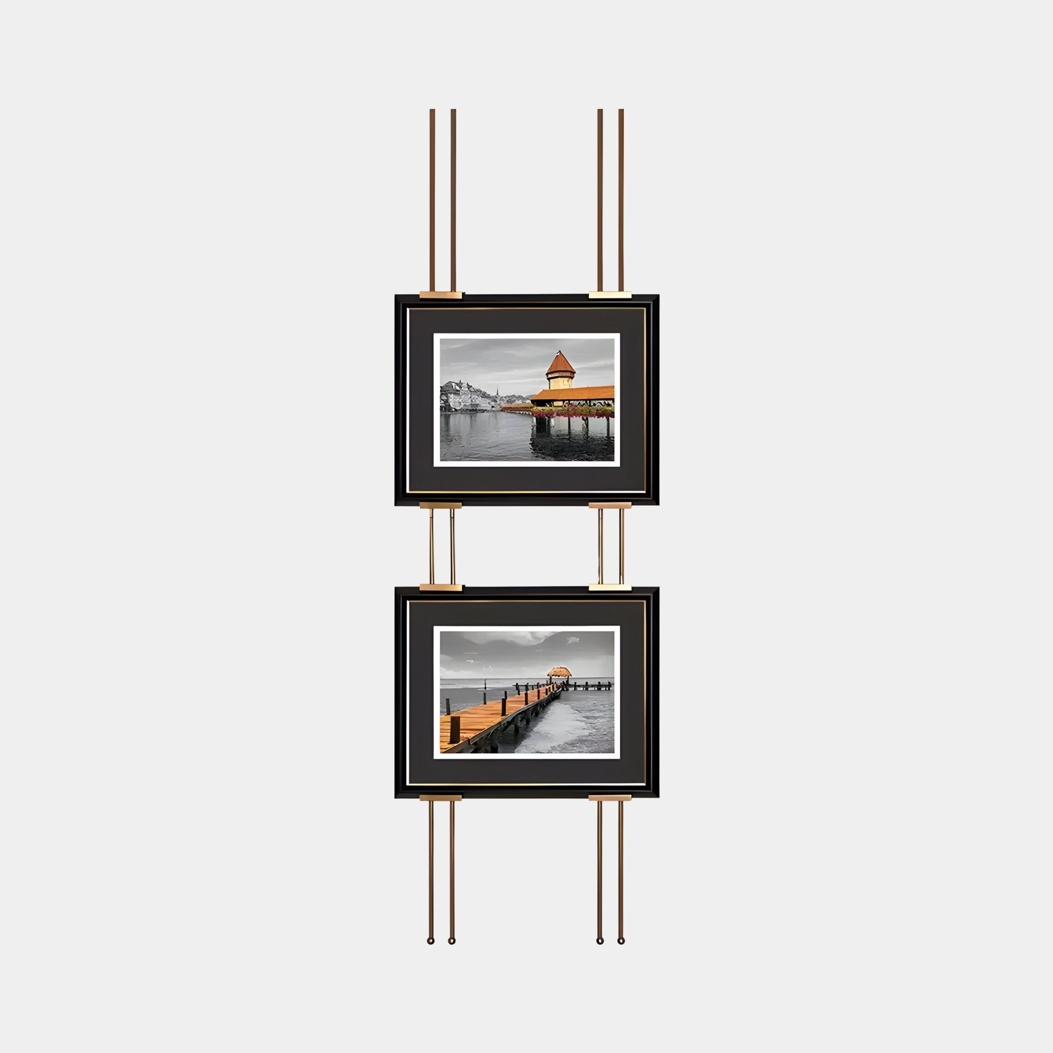 Two black-framed landscape photographs from the Imperia Serene Lakeside View Dual Frame Metal Wall Art by Giant Sculptures are mounted vertically on a minimalist gold rack, featuring a lakeside house above and a wooden pier below for stunning wall decor.