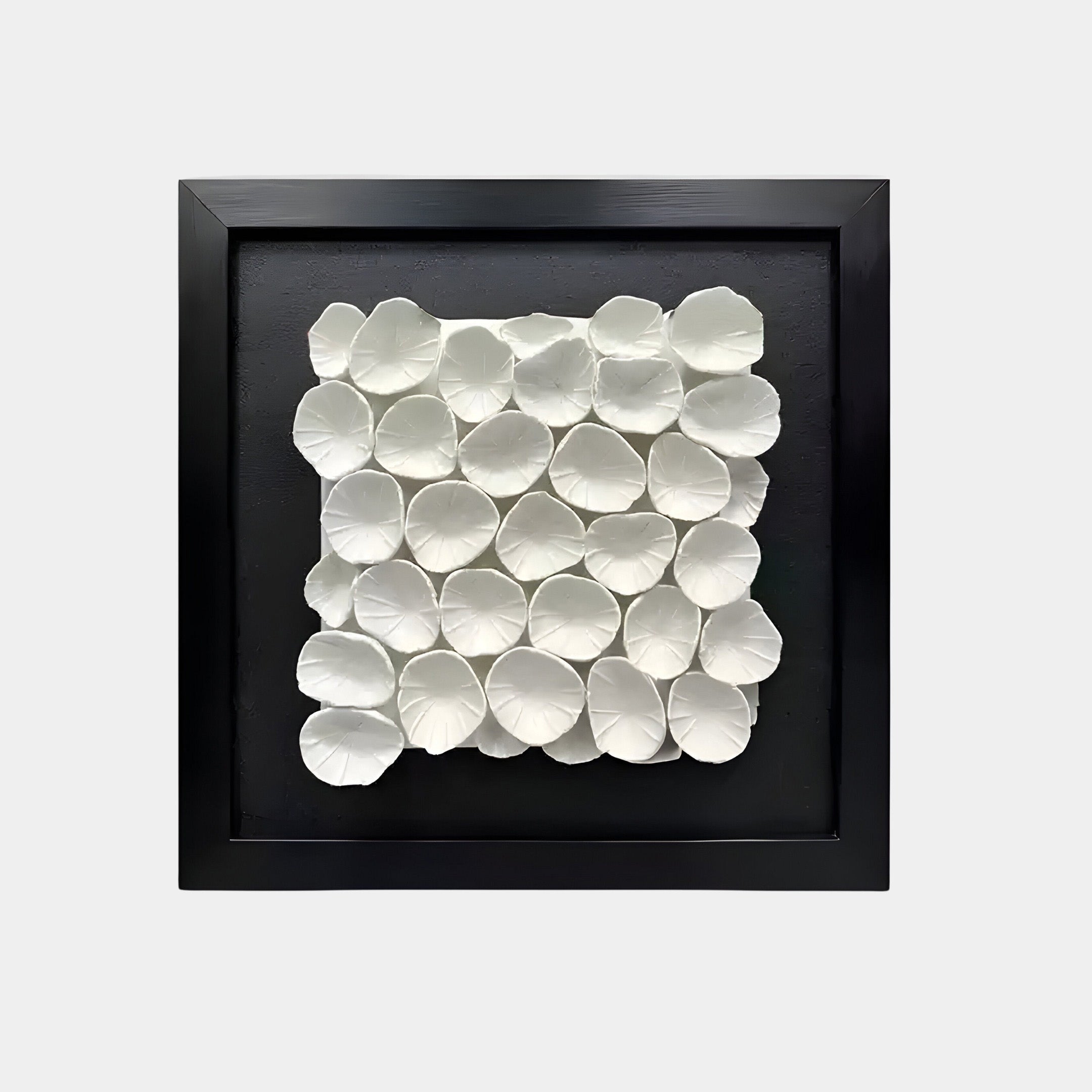 The Giant Sculptures Harmonia 3D Petal Wall Sculpture features white, petal-like ceramic shapes arranged in a neat, overlapping grid on a black background within a square black frame. The floral-inspired motif exudes modern sophistication with its textured pattern.