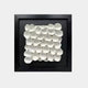 The Giant Sculptures Harmonia 3D Petal Wall Sculpture features white, petal-like ceramic shapes arranged in a neat, overlapping grid on a black background within a square black frame. The floral-inspired motif exudes modern sophistication with its textured pattern.