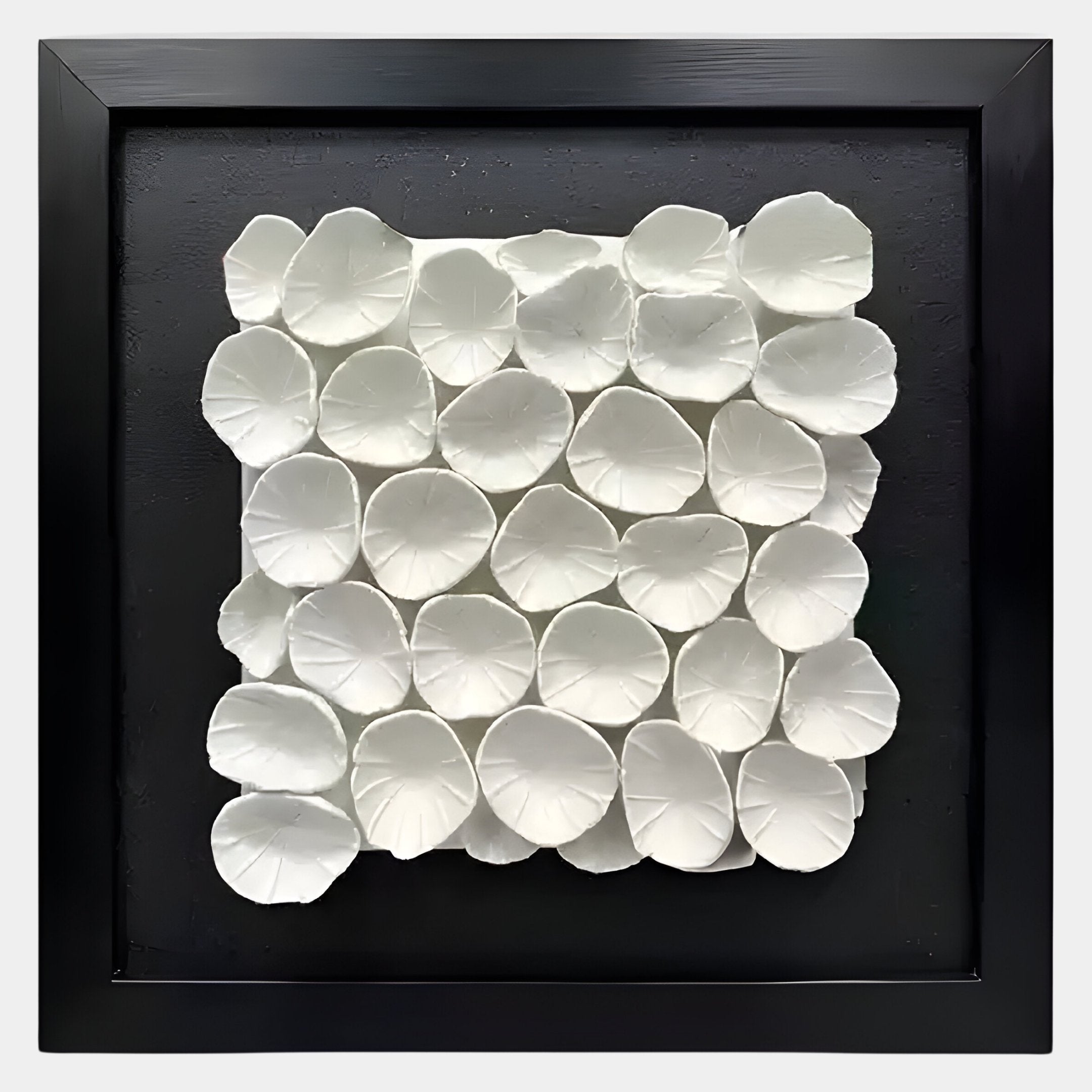 The Harmonia 3D Petal Wall Sculpture by Giant Sculptures features overlapping white ceramic petals with flower-like grooves, elegantly arranged in a grid within a black frame—perfect for modern interiors.
