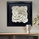 A Harmonia 3D Rose Wall Installation by Giant Sculptures elegantly adorns a wooden shelf with its sculptural layering of white petals. A minimalist face-sketch vase with green branches complements this modern decor, enhancing the refined atmosphere.
.