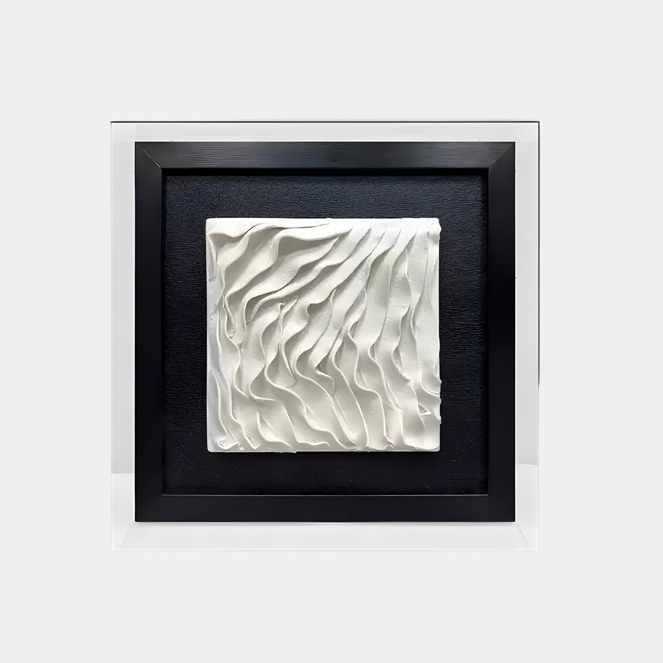 A framed 3D white ceramic artwork featuring flowing, wave-like patterns set against a black background. The design is encased within a sleek black border and is mounted inside a larger white frame, highlighting its textured and elegant appearance.