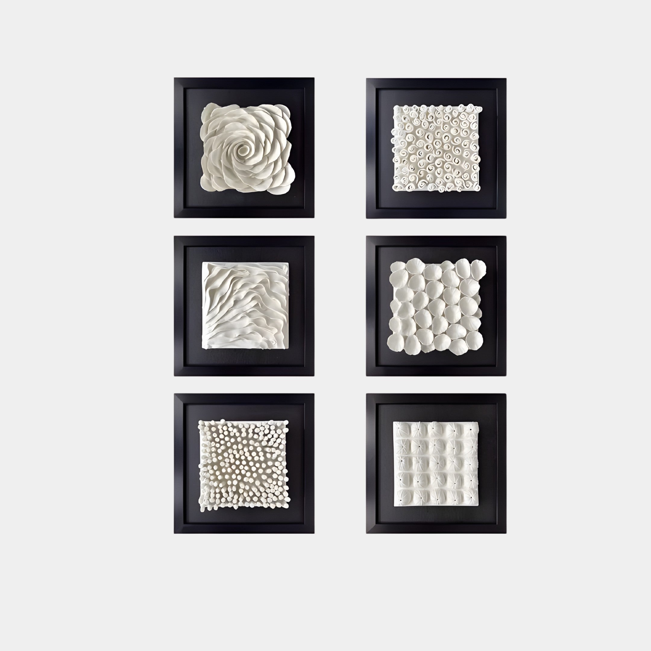 The Harmonia Set by Giant Sculptures features six 3D ceramic wall sculptures in black square frames. Arranged in two vertical columns, each piece exhibits modern designs with textured patterns, from circular forms to abstract waves, adding visual depth against a white background for an elegant touch.