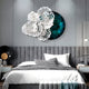 A modern bedroom features a gray padded headboard, black and white bedding, and Giant Sculptures Aurum Flora White Petals Emerald Metal Wall Art above the bed. A sleek pendant light on the right adds elegance.