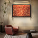 A modern living room showcases the Celestique Prosperity Script Framed LED Wall Art by Giant Sculptures, featuring East Asian characters symbolizing prosperity. A maroon armchair rests beside a tall plant, and a round black coffee table with a book sits in the foreground.