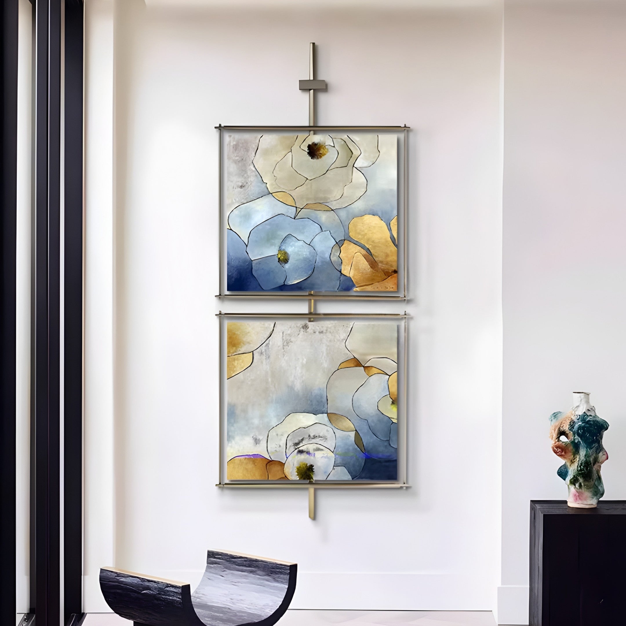 The Vortice Bloom Symphony Floral Dual Panel Wall Art by Giant Sculptures, featuring blue, gold, and white floral designs, is mounted with a modern metal hanger. A black cabinet below displays a colorful sculpture. Nearby, a chair with a curved black and white design enhances the modern aesthetic.