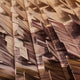 A close-up of the Vista Sunset Urban Landscape Carving Wall Art by Giant Sculptures features layered sheets with wood-like textures in brown and beige, arranged at various angles. It captures architectural elegance with a dynamic pattern.