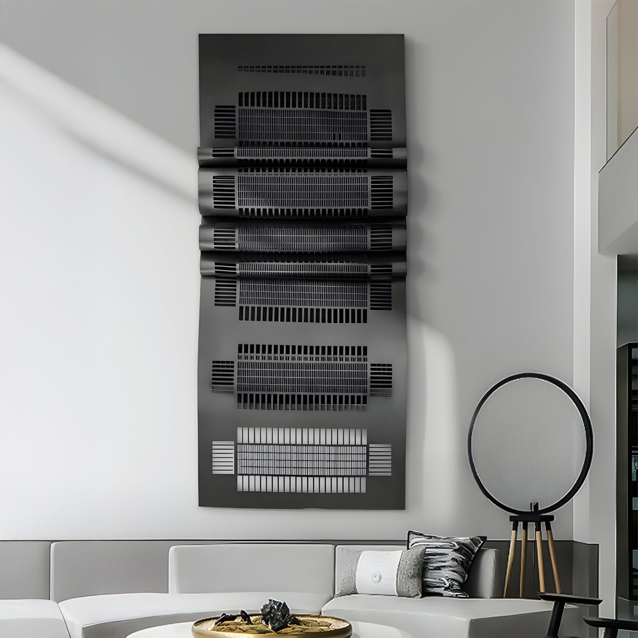 A sleek, modern living room with a white sectional sofa and patterned cushions boasts the Strata Black Vertical Folded Grid Metal Wall Art by Giant Sculptures above. A round lamp with a wooden tripod base stands nearby, adding contemporary flair to the minimalist decor.