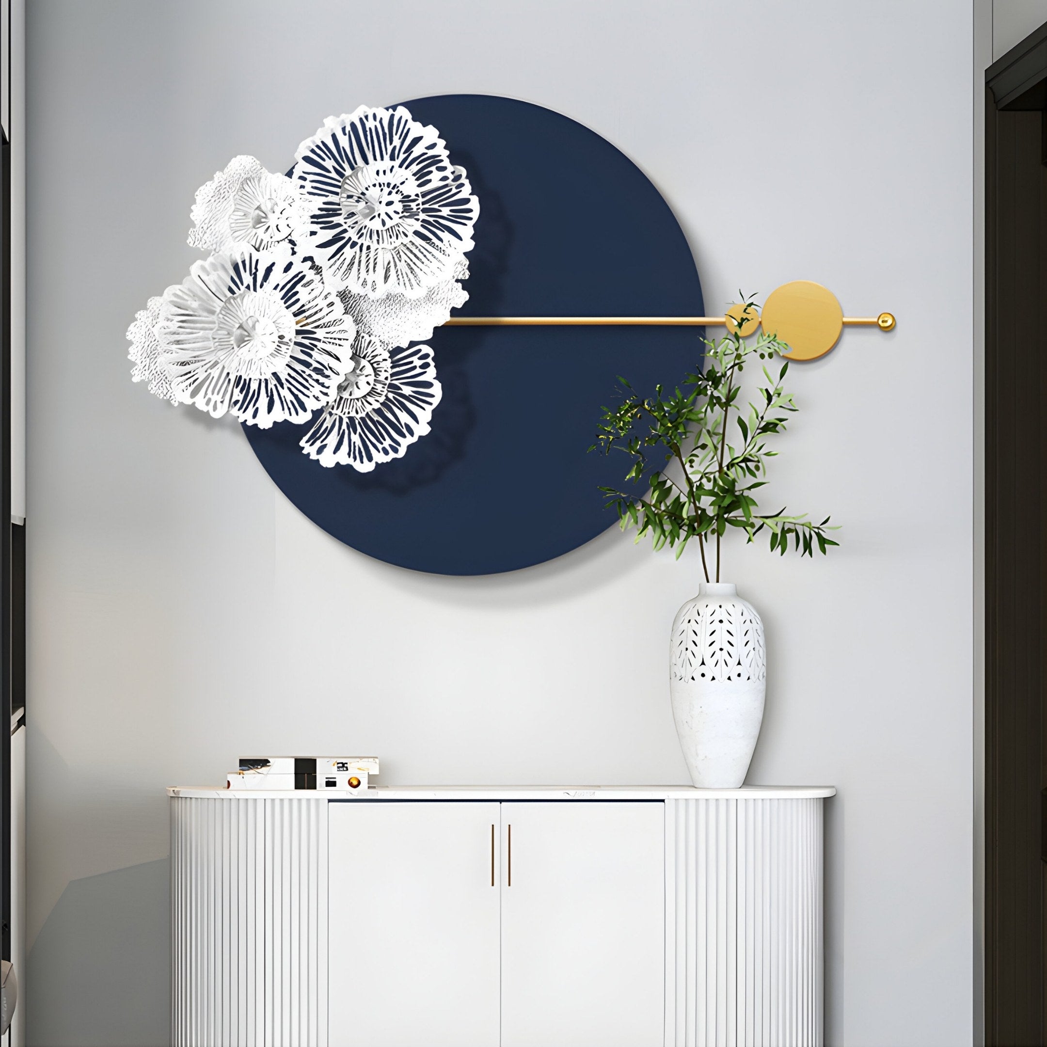 The Blossom Halo Midnight Blue Round Floral Decorative Wall Art from Giant Sculptures, featuring white floral cutouts and a gold rod, is mounted above a white vase with green branches on a white cabinet against a gray wall, adding elegance to modern interiors.