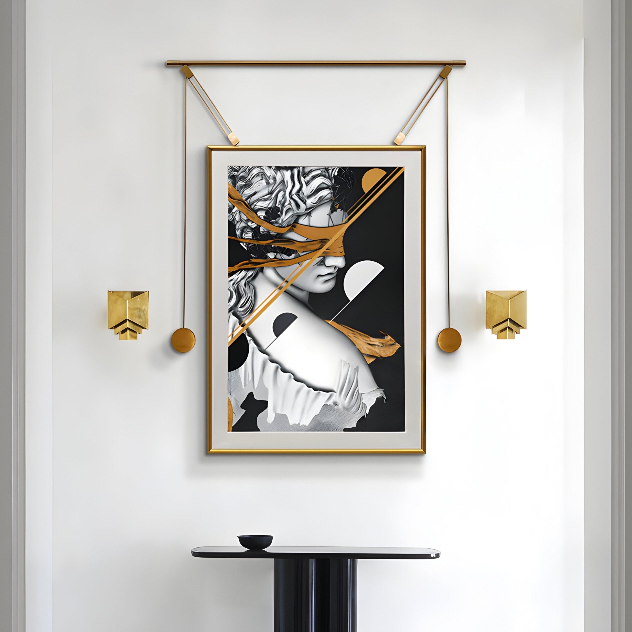 The Eterna Classics Athena Replica Portrait Golden Frame Wall Art by Giant Sculptures, featuring abstract shapes and a partially visible face in black, white, and gold tones, hangs on a white wall suspended by ropes. Its flanked by gold sconces with a small black table and bowl beneath.