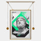 The Eterna Classics Zeus Replica Portrait Golden Frame Wall Art by Giant Sculptures features a bearded statue head with geometric shapes and vivid green accents, hanging from a gold rod—contemporary charm on a plain white backdrop.