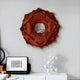 A contemporary living room showcases the Giant Sculptures Sculptura Mirror, a terracotta red floral round metal wall art. Below, a white console holds framed art and a clear glass bubble sculpture. A white table is partially visible in the foreground.