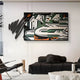 A modern living room with a black leather couch, cushions, marble coffee table, and Graffio Graphic Edge Fragmented Canvas Wall Art by Giant Sculptures on the wall. The piece showcases geometric shapes and bold colors. A black chair is partly visible on the left.