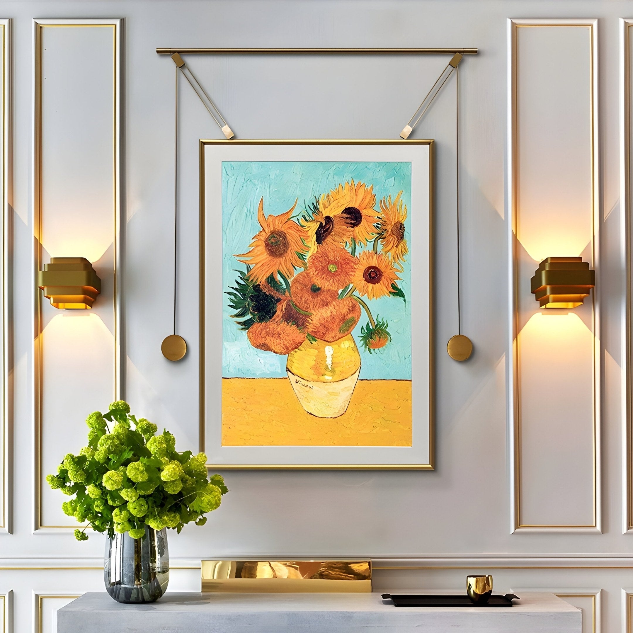 The Reverra Vibrant Sunflowers Hanging Frame Wall Art by Giant Sculptures adorns a paneled wall with gold sconces. Below, a table displays a glass vase with green flowers and a book, adding to the stylish, artistic ambiance that complements the stunning wall art.