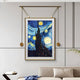 The Reverra Starry Night Classic Hanging Frame Wall Art by Giant Sculptures adorns a modern gray wall, showcasing swirling blue skies and bright yellow stars. A beige couch with blue and white pillows sits beneath it, accompanied by a small white table.