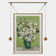 The Reverra White Blossoms Hanging Frame Wall Art by Giant Sculptures features white flowers in a green vase, displayed on a light green background with a decorative hanging frame, gold picture light above, and two gold weights at each side.