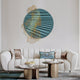 A modern living room features a white sofa and round coffee tables, complemented by the Giant Sculptures Auramesh Teal Blue-II Metal Winged Circular Geometric Wall Art on the left. Neutral-colored cushions and a decorative bowl with spherical objects rest on the tables.