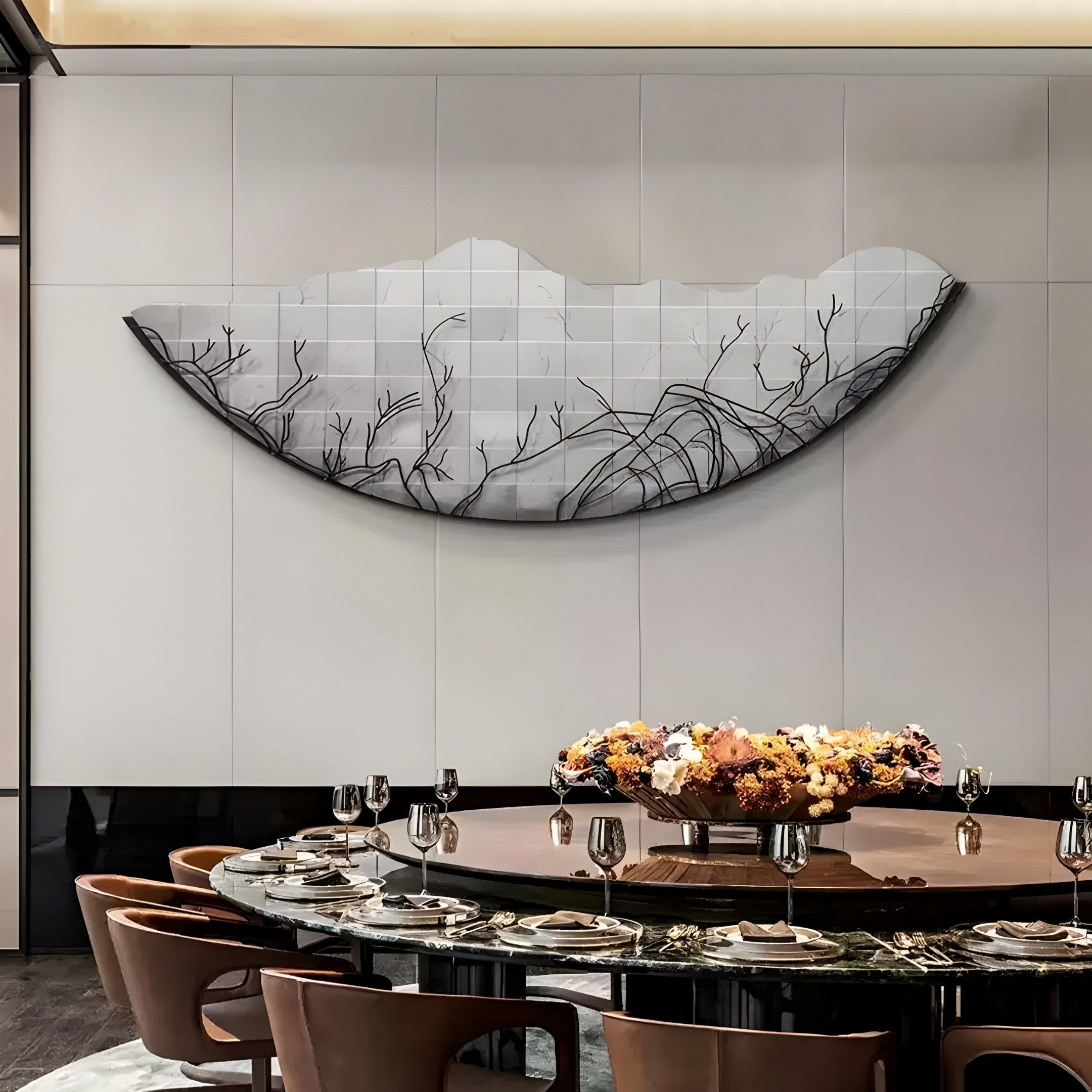 A modern dining area has a round table set with plates and glasses, surrounded by brown chairs. An Arcana Grey Abstract Branch Mosaic Half-Moon 3D Wall Art by Giant Sculptures adds modern artistry to the light wall with its fragmented black and gray half-circle design.