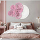 A contemporary bedroom features a beige bed with patterned pillows and neutral bedding. The wall showcases the Fleur Halo White Round Pink Metal Floral Decorative Wall Art by Giant Sculptures, complemented by a large mirror, soft lighting, and minimal decor for an elegant touch.