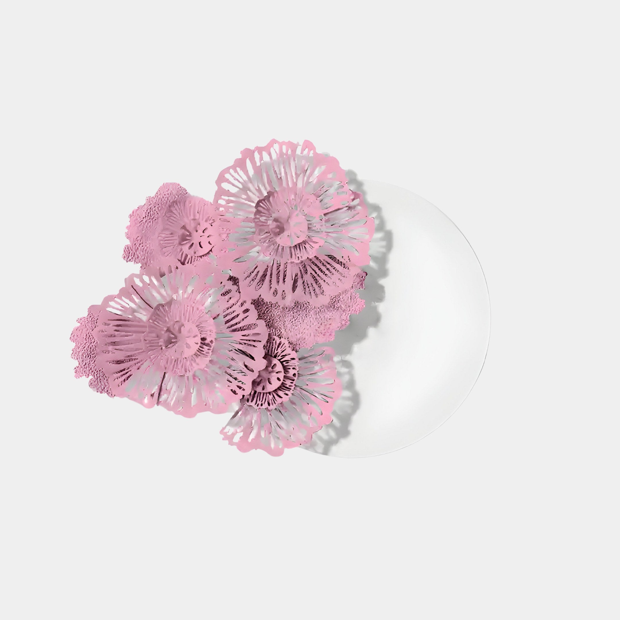 The Fleur Halo White Round Pink Metal Floral Decorative Wall Art by Giant Sculptures features a cluster of intricate pink floral patterns on a white plate against a light gray background, exemplifying contemporary design with its delicate design casting subtle shadows.