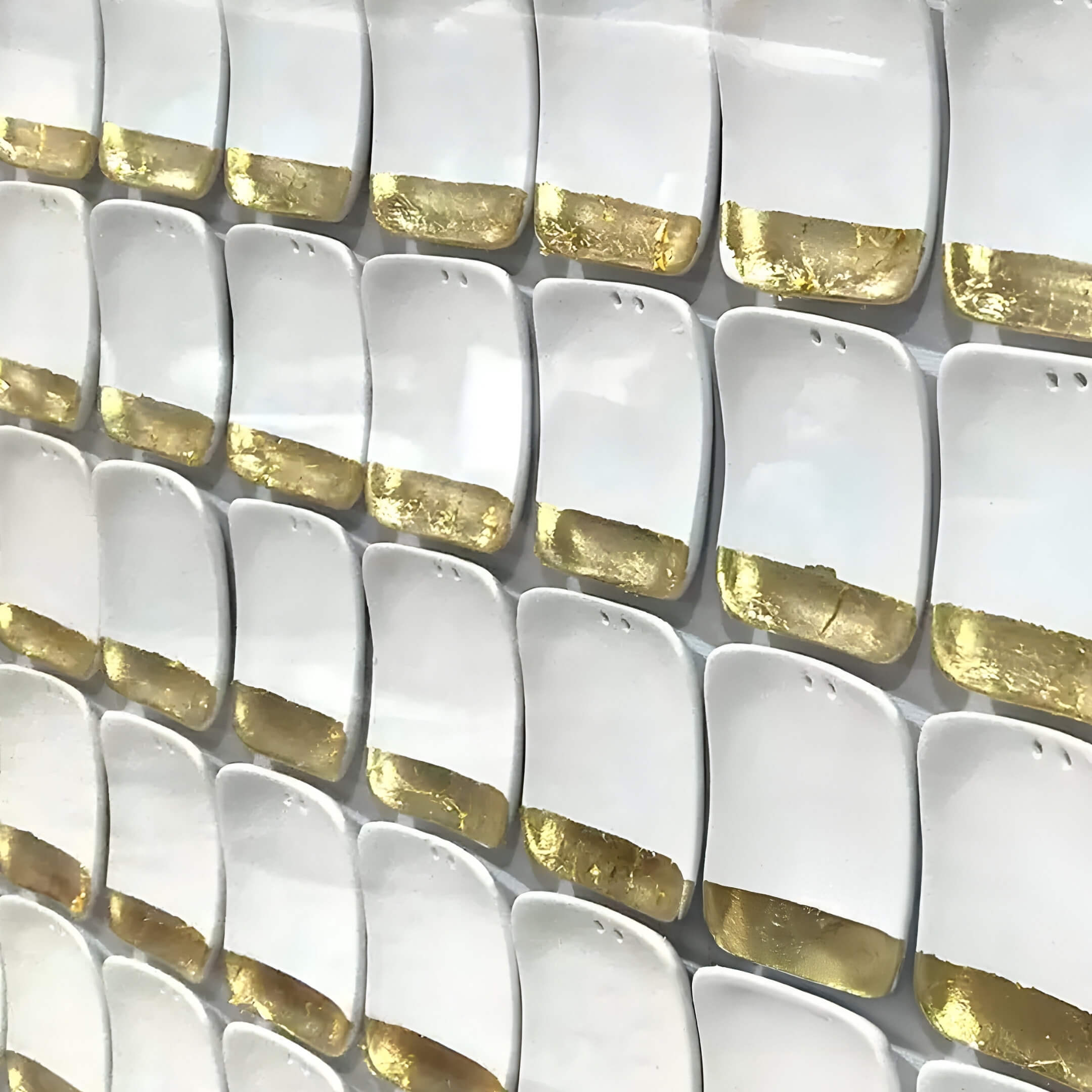 A wall display of Lyselle 3D Ceramic Wall Art by Giant Sculptures features white rectangular tiles with golden sections at the bottom. Theyre arranged neatly, creating a beautiful pattern highlighted by hand-applied gold foil accents.