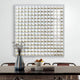 A modern dining room showcases a wooden table with brown chairs, a decorative vase of dried plants, and a fruit bowl on two stacked books. Giant Sculptures Lyselle Wall Art with hand-applied gold foil accents in gold and silver tones adorns the white wall.