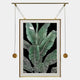 The Glacia Green Botanical Crystal Hanging Framed Wall Art by Giant Sculptures features vivid banana leaves with white veins on black, suspended from a gold rod with weighted cords—a bold, modern botanical piece.