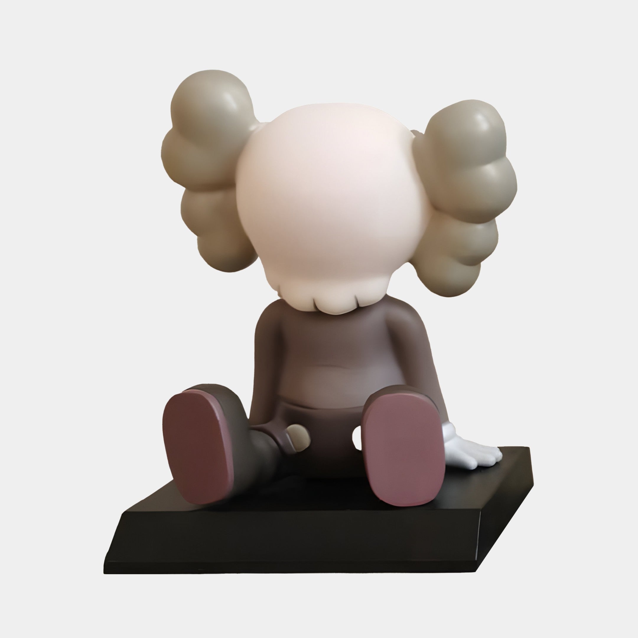 The Hazelnut Brown I Iconify Bobblehead Figure by Giant Sculptures boasts a cartoonish style, resting on a black platform. With a round pale head, large grey ears, dark grey body, bright pink soles, and white gloves, this 10cm minimalist resin figure embodies a playful essence.