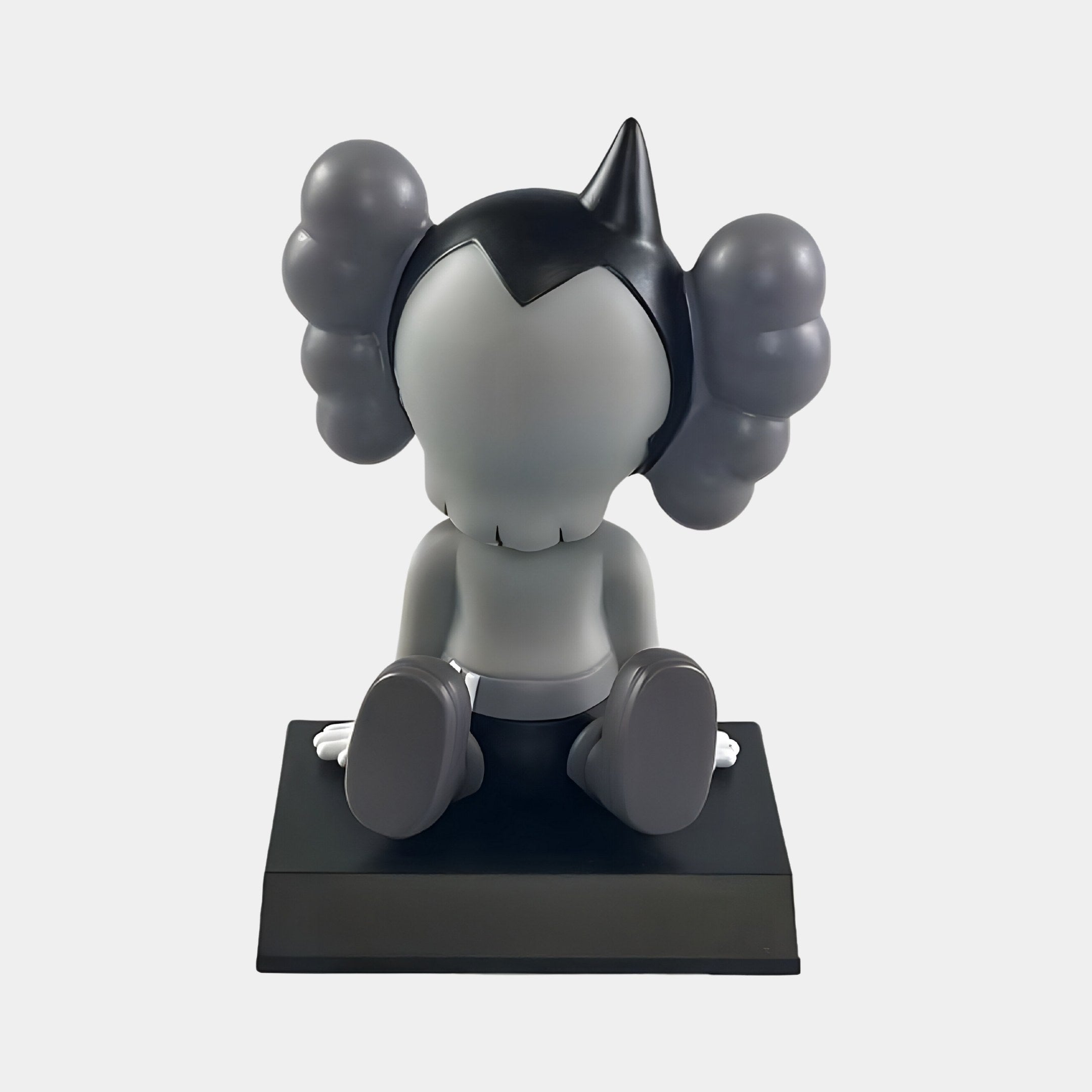 The Slate Grey Iconify Bobblehead Cosmic Boy Figure by Giant Sculptures is a 10cm monochromatic vinyl piece ideal for collectors, featuring a cartoonish design with a large head, curly attachments, and playful charm as it faces away on a black base with gray and black body, oversized feet, and gloved hands.