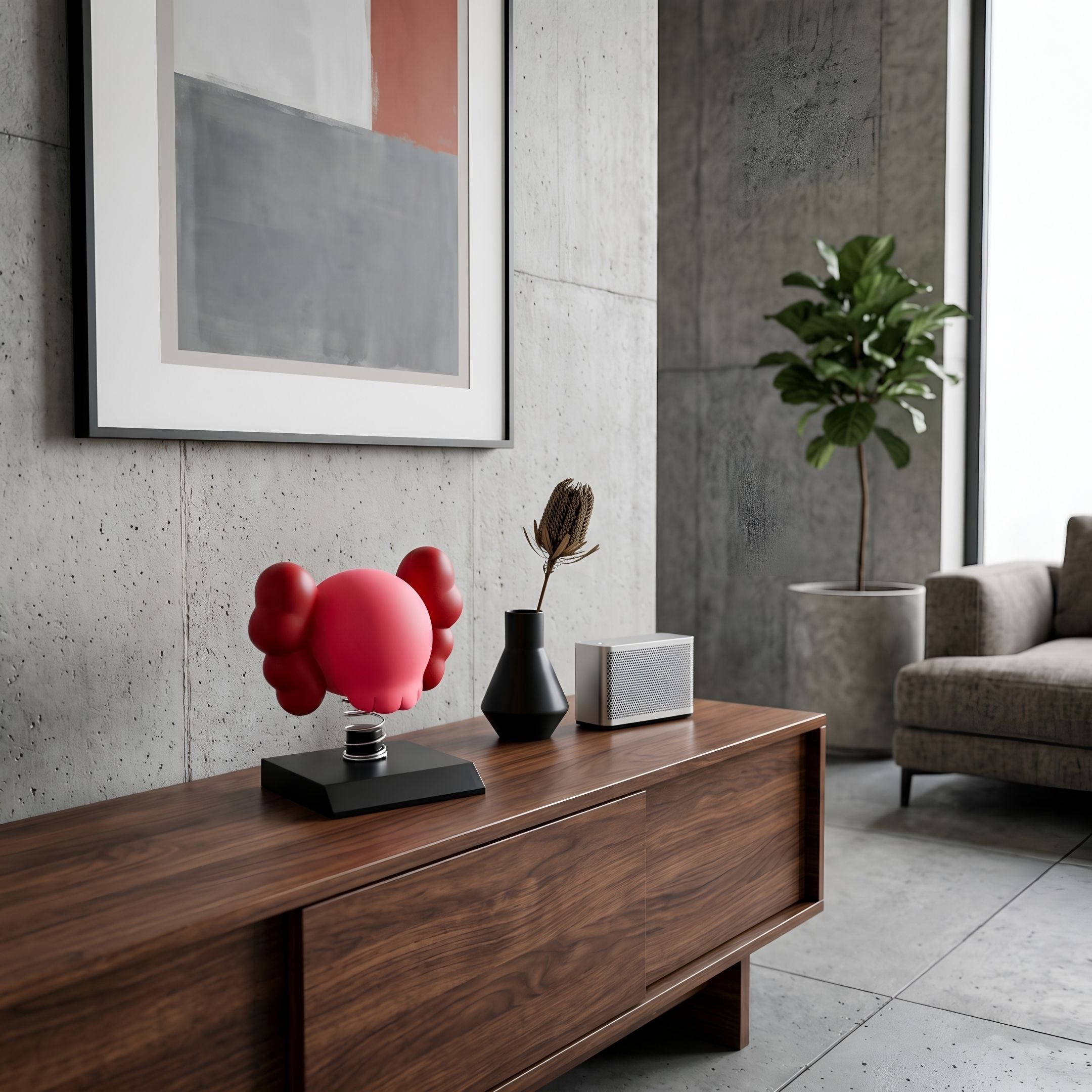 Blush Ruby Iconify Bobblehead Figure on a black base atop a walnut sideboard, styled with a dark vase, dried stem, and speaker in a modern living room.