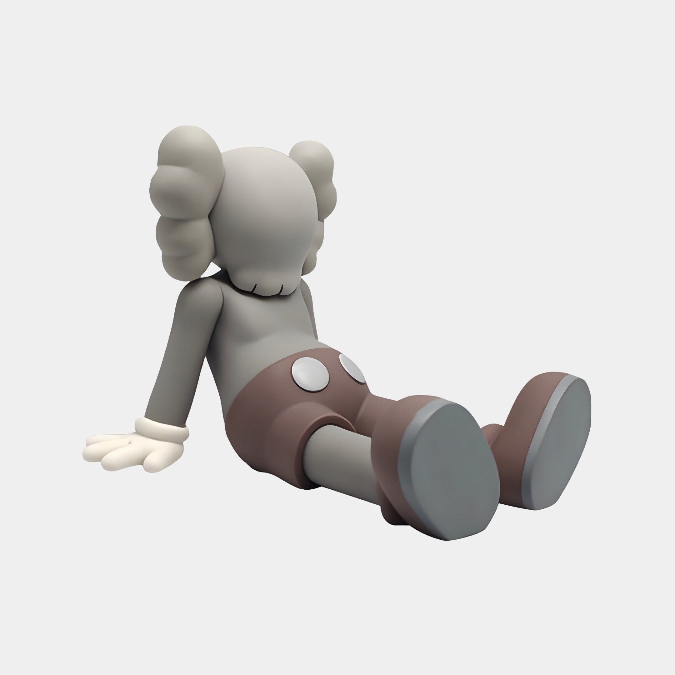 The Warm Graphite Iconify Daydream Sculpture by Giant Sculptures features a cartoonish gray figure with large round ears, white gloves, and brown shorts sitting relaxedly against a plain white background—perfect for minimalist decor. The sculpture is 85cm tall.