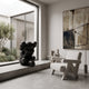 Obsidian Black Iconify Sorrow Sculpture, 92cm, seated figure with hands covering face, shown on a concrete window ledge beside a boucle armchair and abstract wall art.