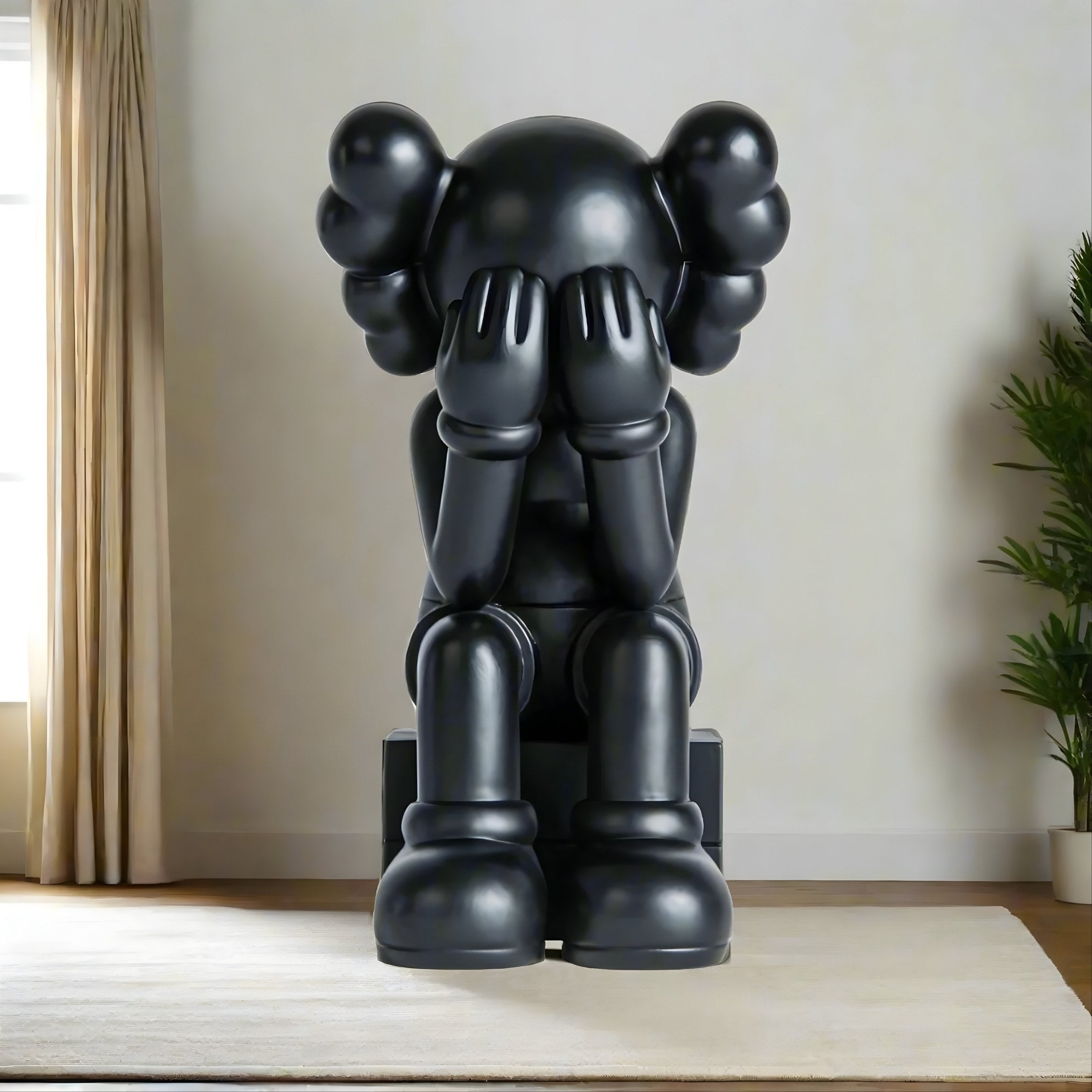 The Midnight Black Iconify Melancholy Sitting Sculpture by Giant Sculptures, at 110cm, is a cartoonish figure with gloved hands covering its face and balloon-like ears. It perfectly complements a minimalistic room with light curtains and greenery.