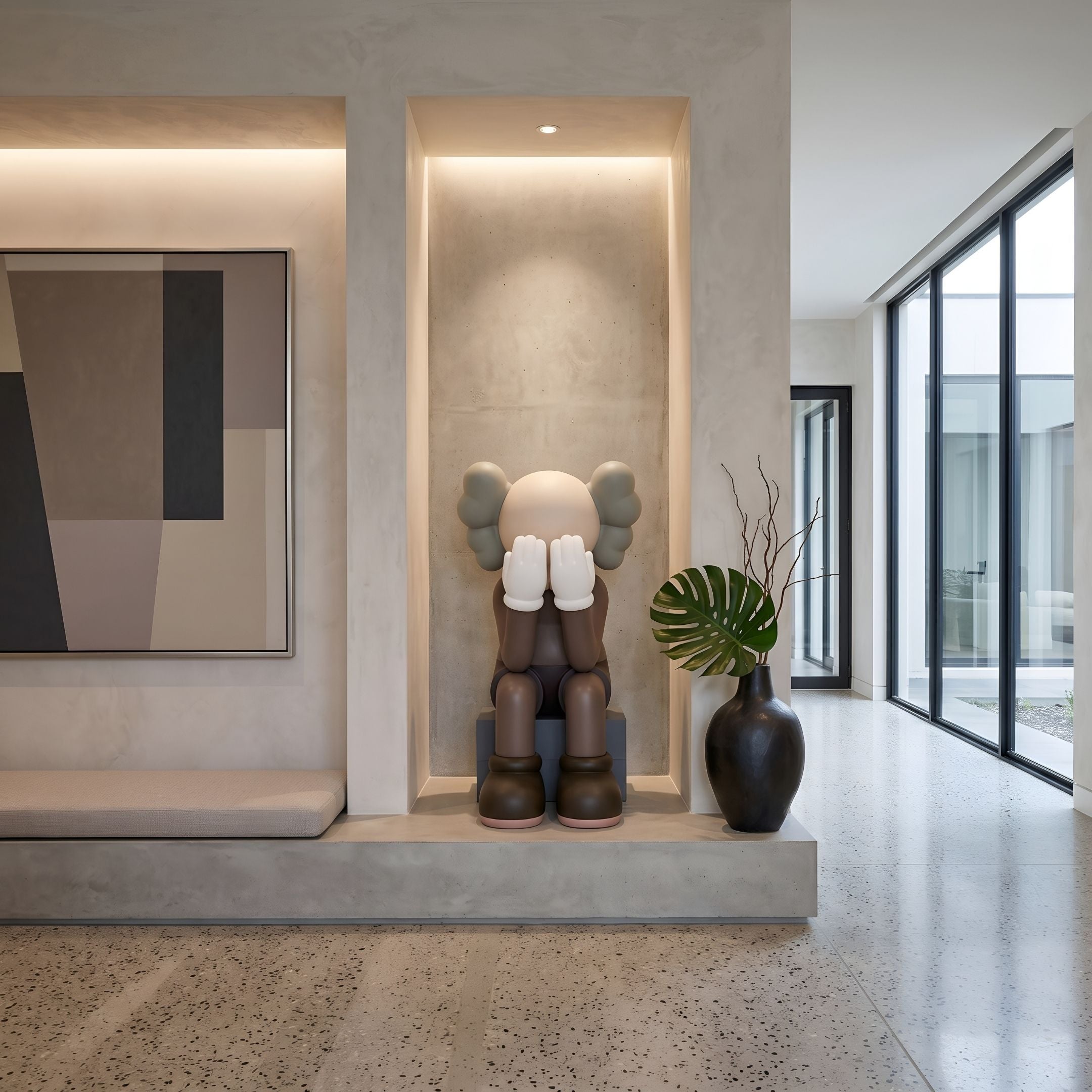 Hazelnut Brown Iconify Melancholy Sitting Sculpture, 110cm, seated on a black plinth in a wall niche beside a dark vase in a modern entryway.