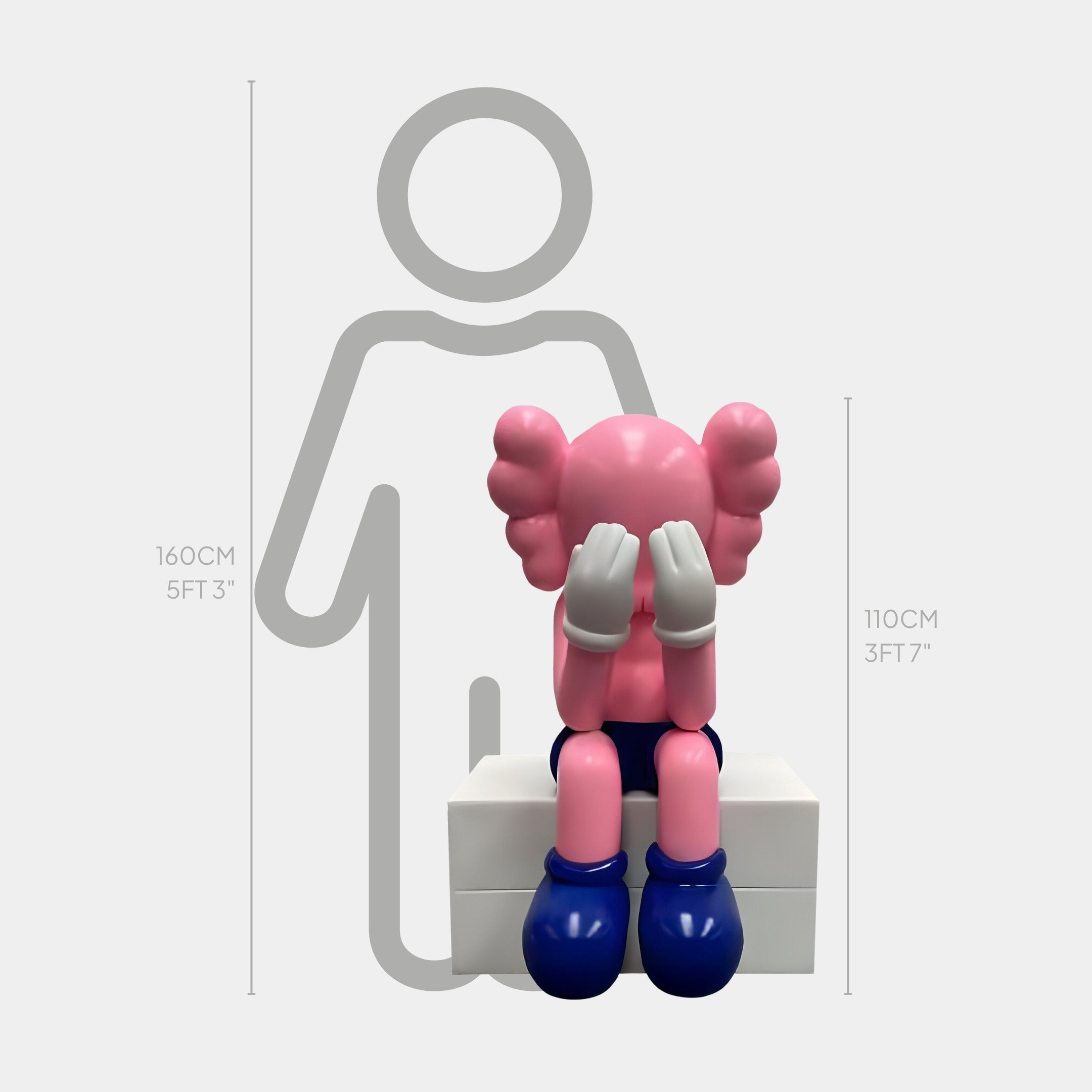 The Petal Pink Iconify Melancholy Sitting Sculpture by Giant Sculptures features a cartoon figure on a white block, hands over its face. The 110 cm (3 ft 7 in) sculpture is compared to a 160 cm (5 ft 3 in) silhouette.